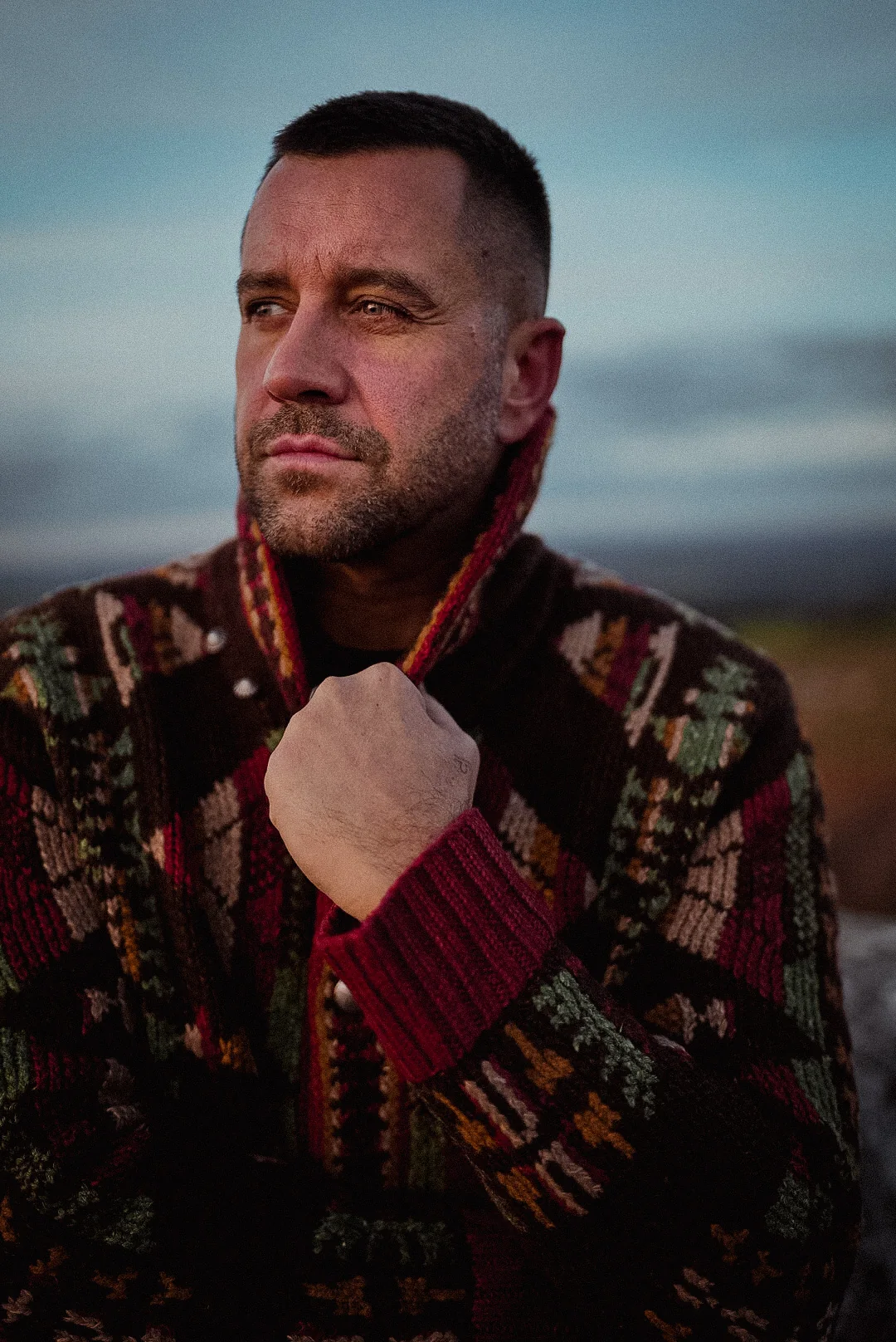 Porträt von Ben Kauer im gemusterten Strickpullover vor dem Abendhimmel